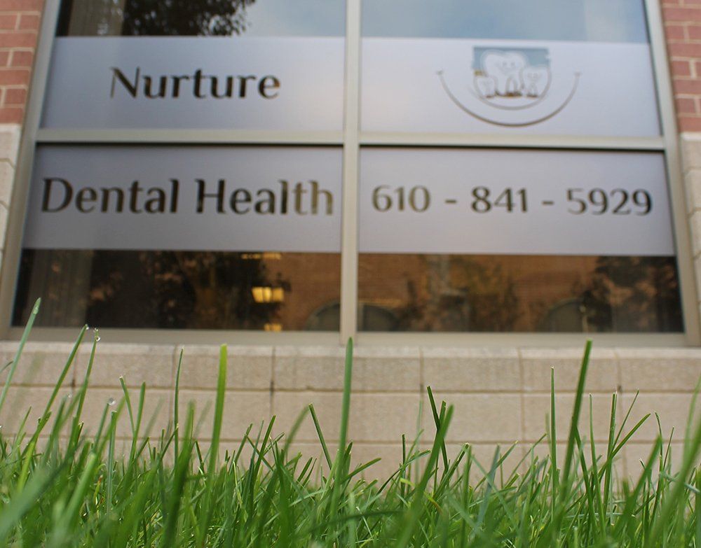 Window film of Nurture Dental Health's Dental office, view from the grass on the ground outside the window.