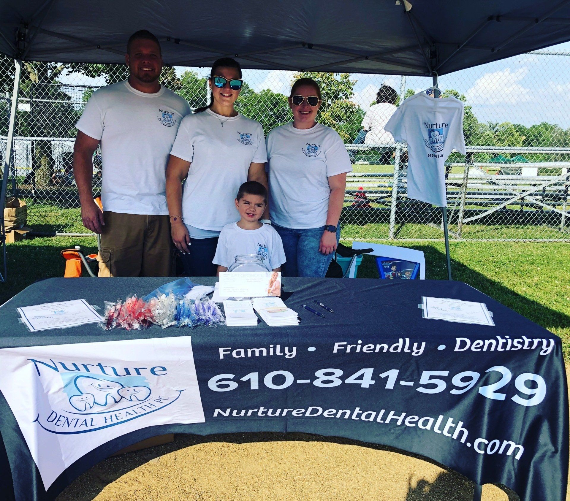 Three adults and a child standing behind a table for Nurture Dental Health promoting a raffle for Free Teeth Whitening and toothbrushes