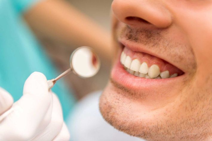 Man's teeth being examined by a dentist with a mirror, in a dental office.