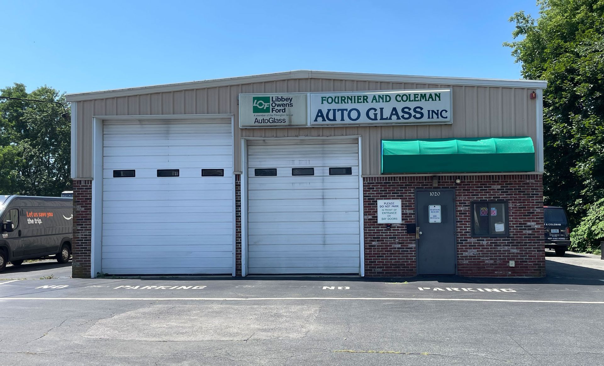 Exterior of Foshee and Coleman Auto Glass Inc. building with two garage doors, small brick-faced office, and parking spots on a sunny day.