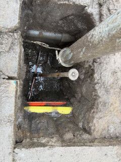 Stone utility pit with exposed pipes, valves, and a yellow-red measuring tool inside.