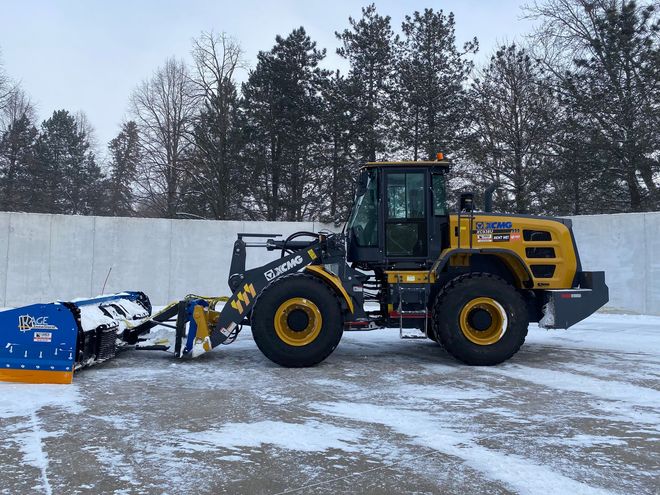 Yellow snowplow with a blue blade clears snow.