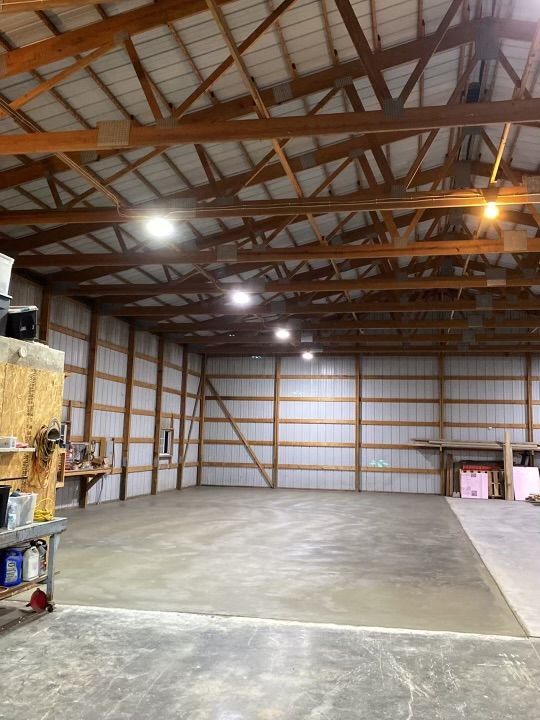 An expansive, empty workshop with high wooden truss ceilings, bright overhead lights, and smooth concrete floors.