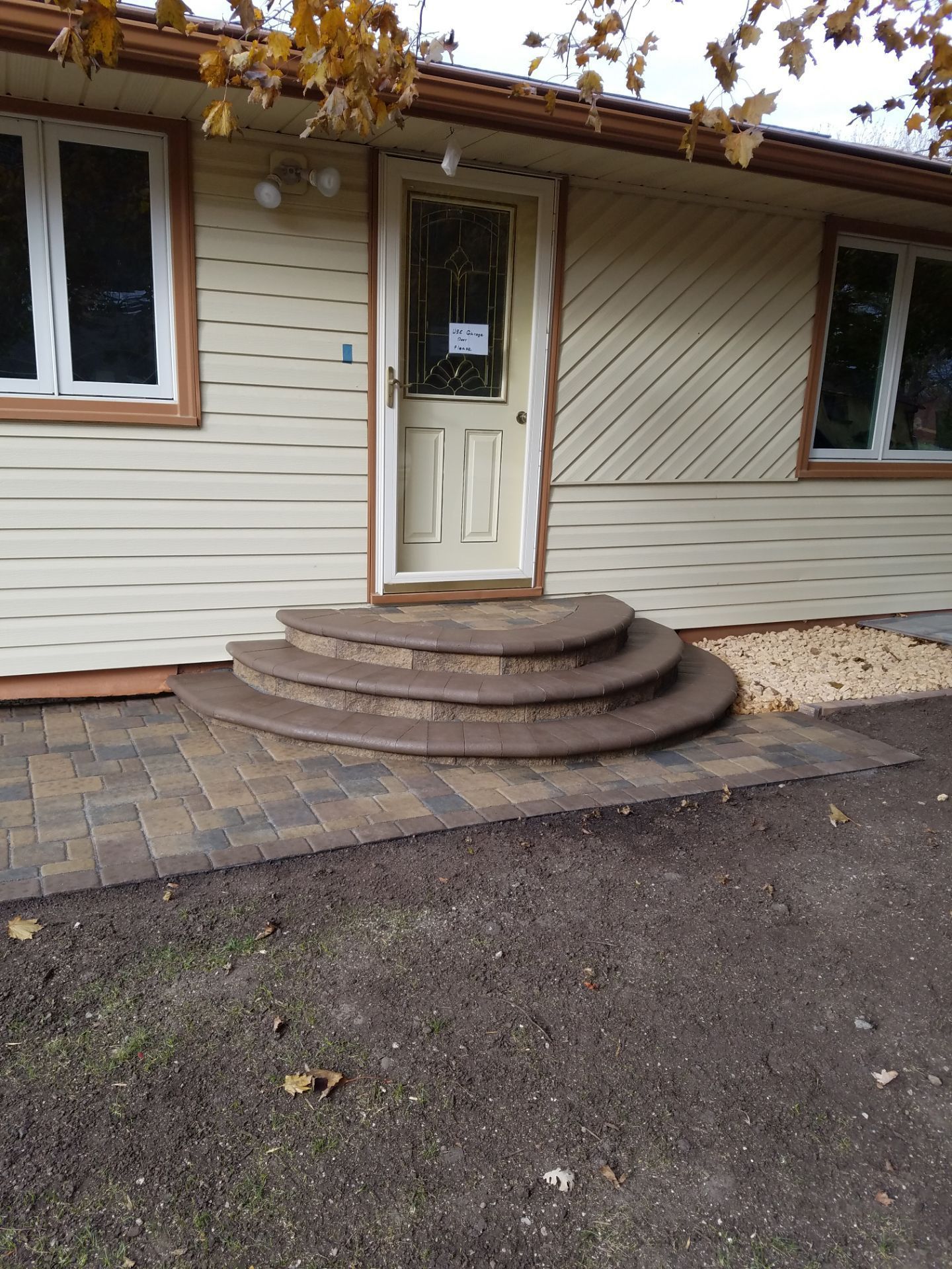 A cream-colored house exterior with three curved stone steps leading up to a front door above a stone paver patio.