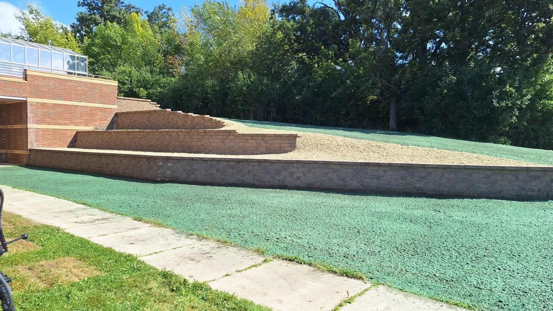 Brick steps and retaining wall beside a sloped lawn and paved walkway under trees.