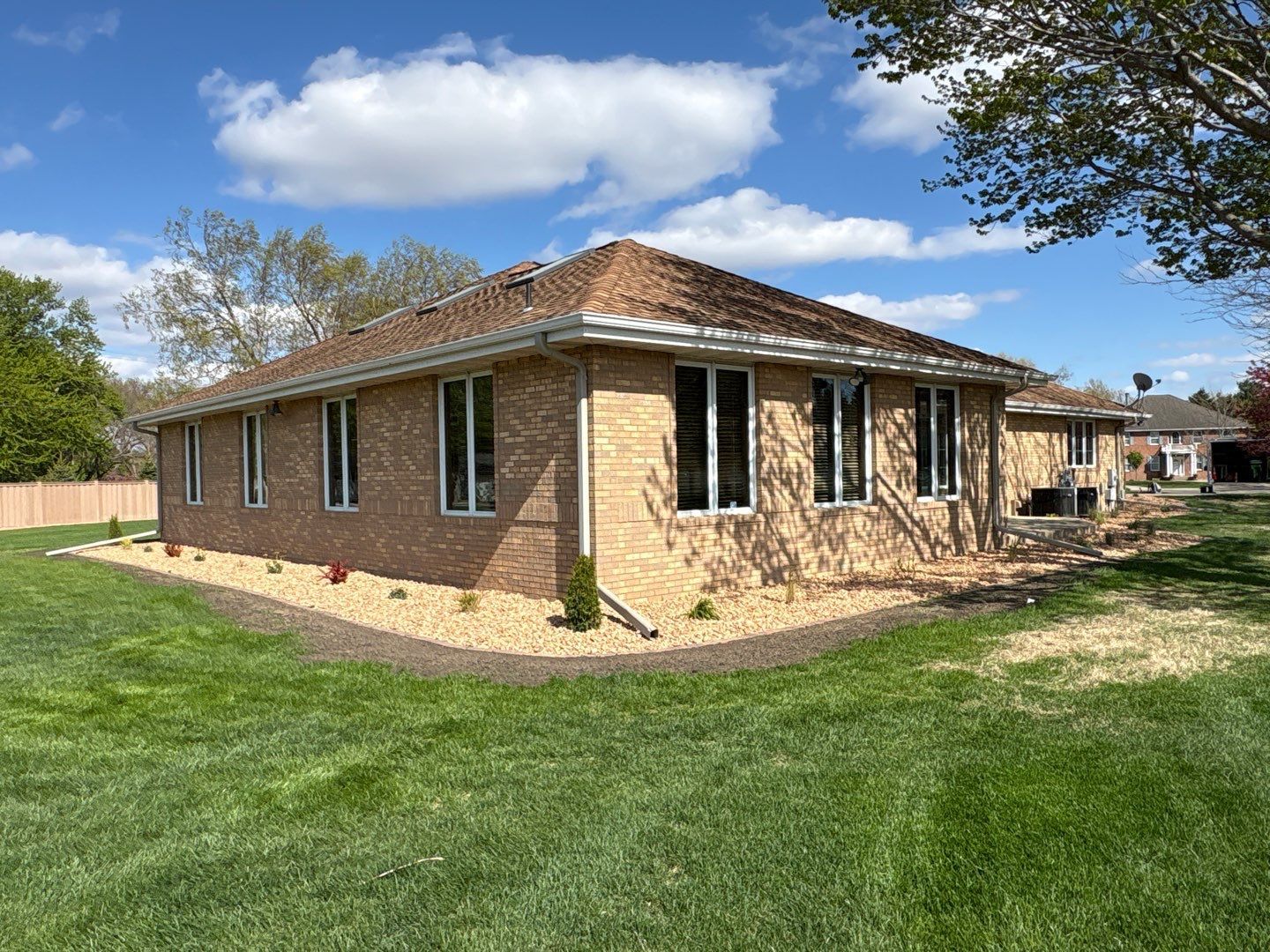 Single-story brick house with a tiled roof, windows, and a large grassy yard under a blue sky