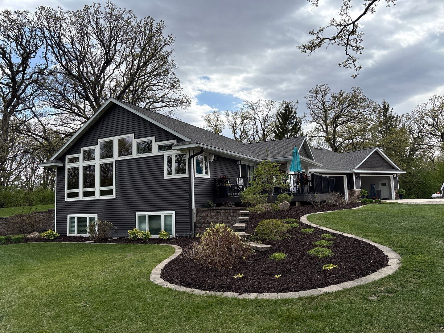 Dark gray house with white trim, curved mulch bed, and green lawn under cloudy sky