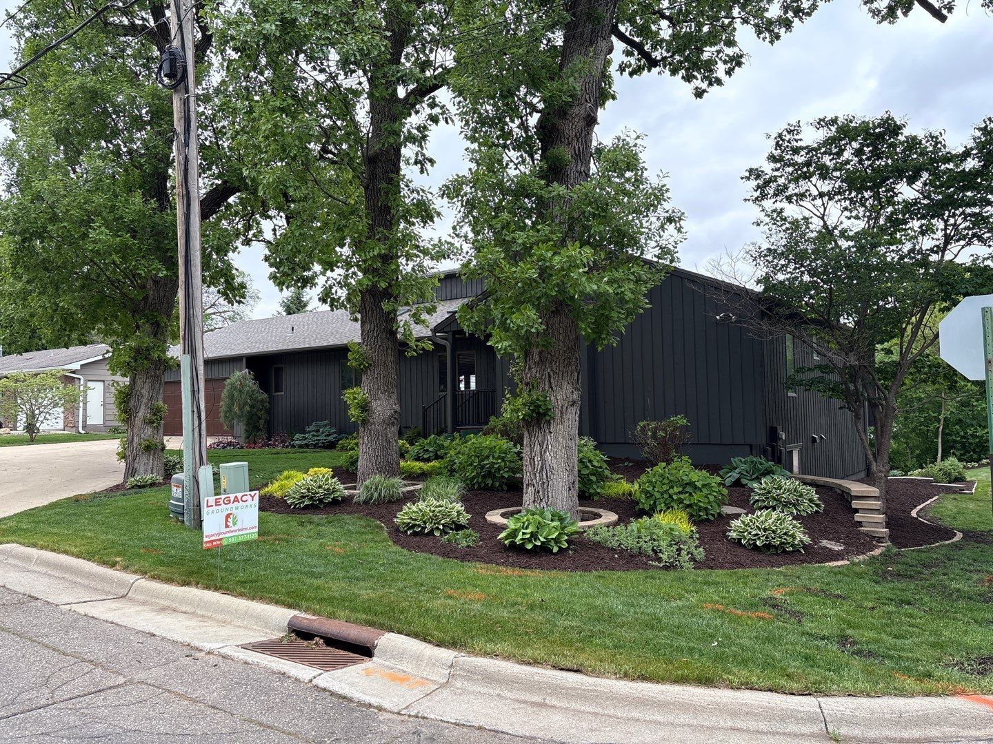 Black house with landscaped yard, trees, and curbside street view