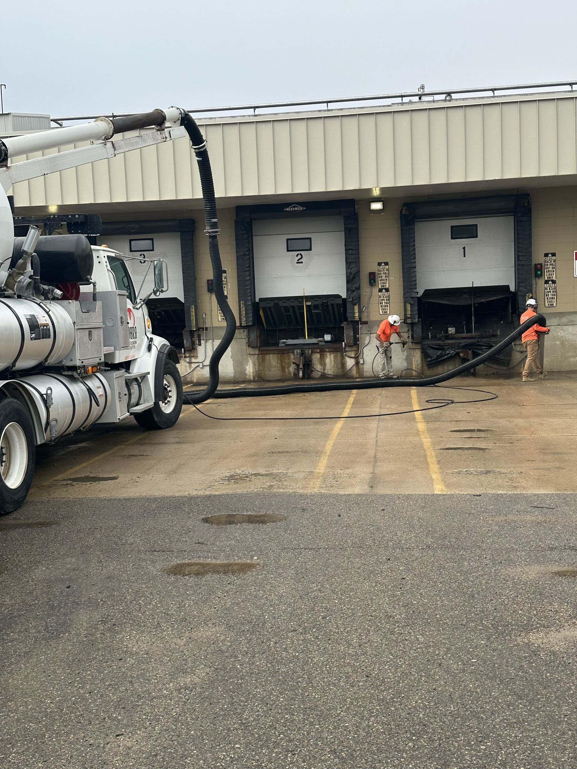 Truck at industrial loading docks with wet pavement and hoses connected to bay doors