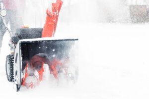 A person operates a bright red snowblower, clearing deep snow on a white, winter day.