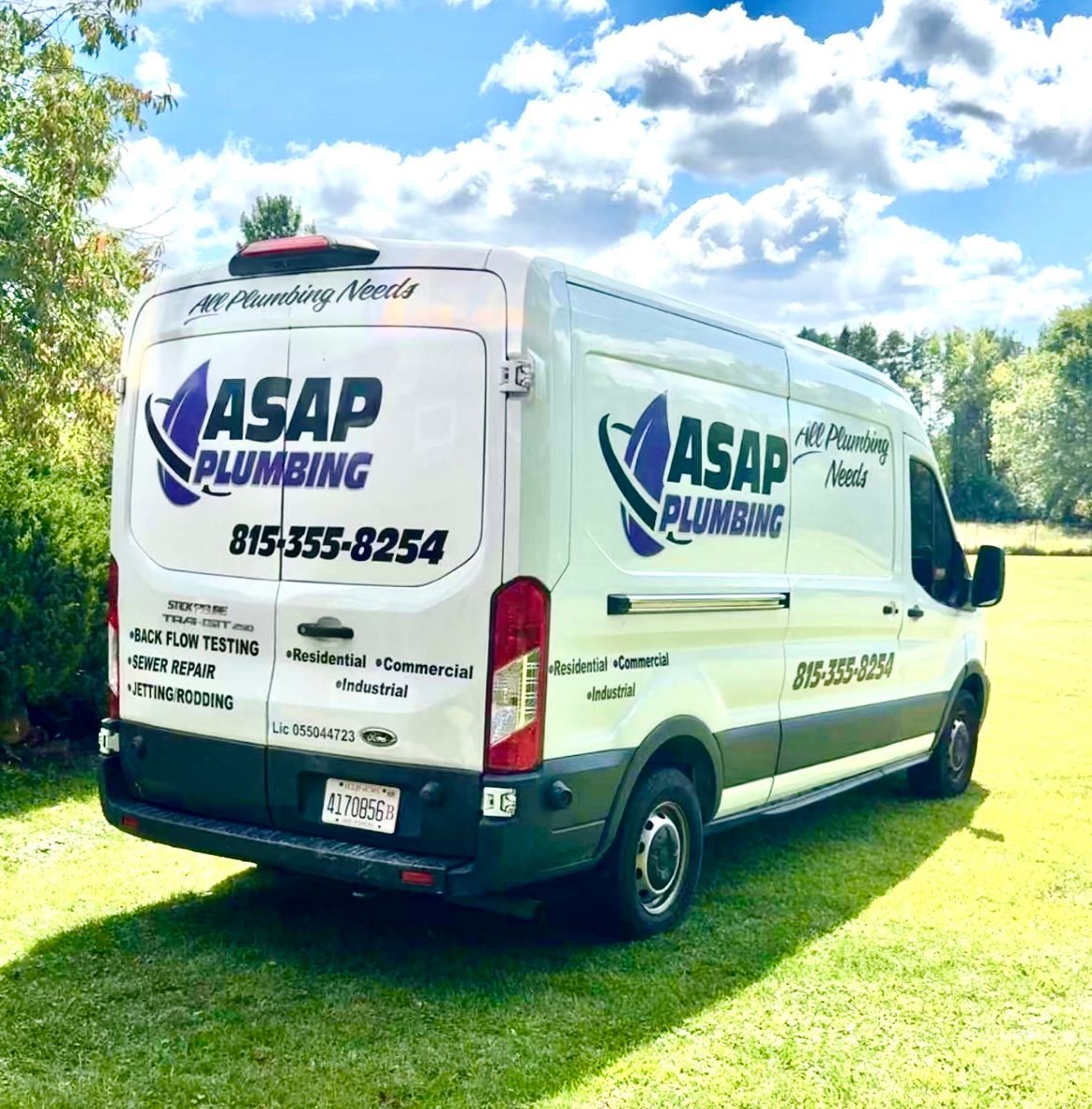 White ASAP Plumbing van parked on green grass, back doors open, with logo and phone number.