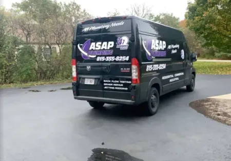 Black ASAP Plumbing van parked on a wet driveway with business info on the side.
