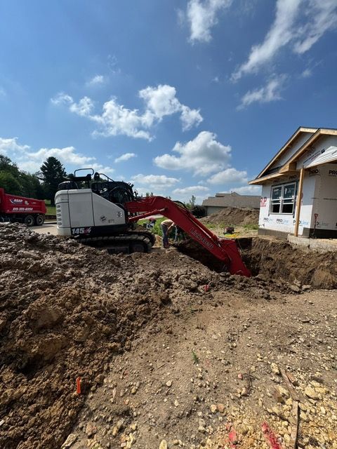 An excavator digging near a house under construction on a sunny day.