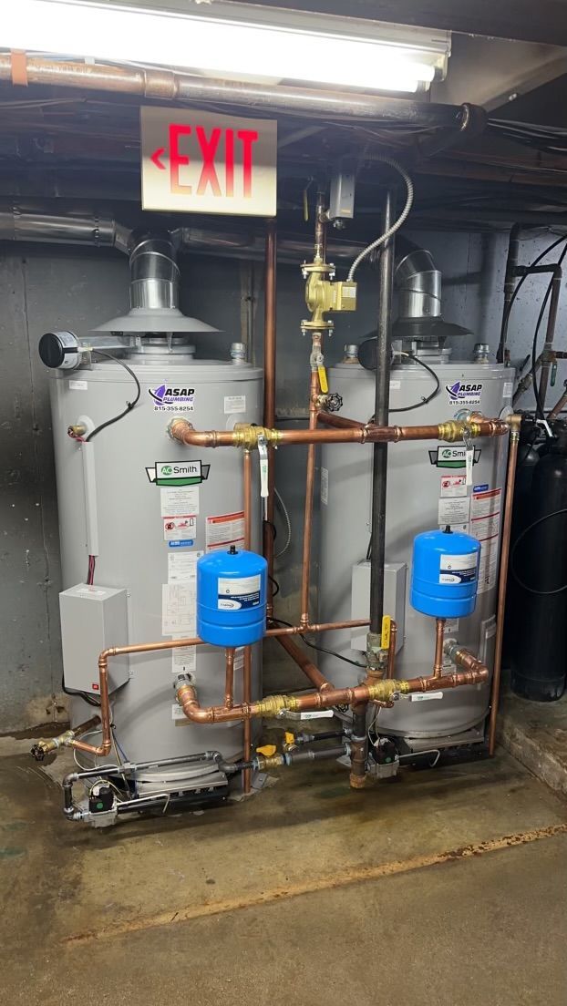 Two vertical water heaters with copper pipes and blue expansion tanks, set in an industrial room.