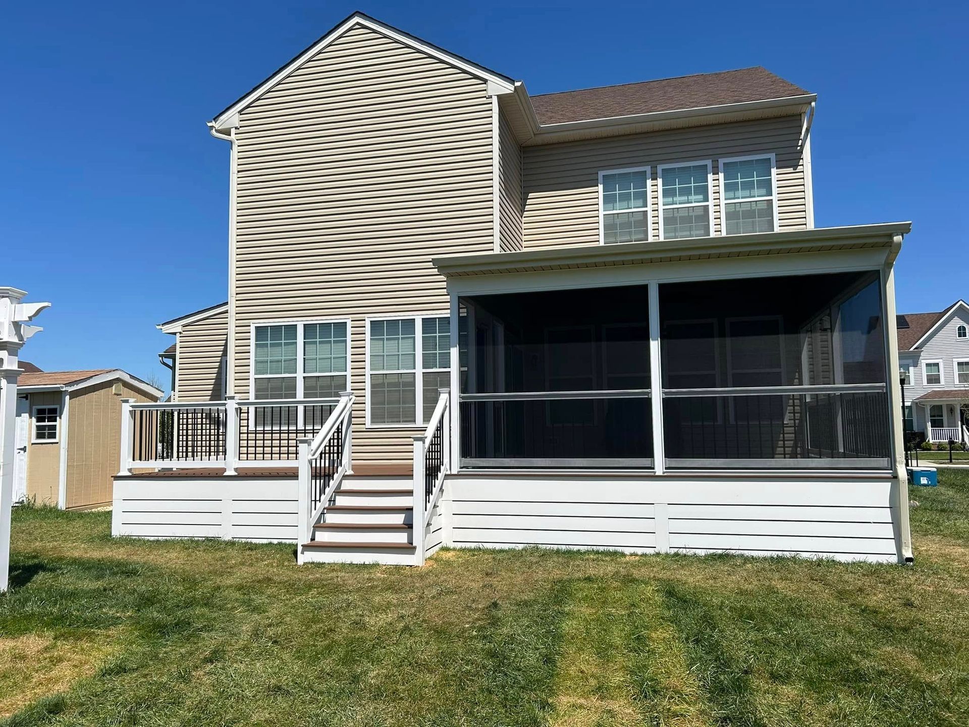 Back of a two-story beige house with a screened porch and wooden deck; blue sky.