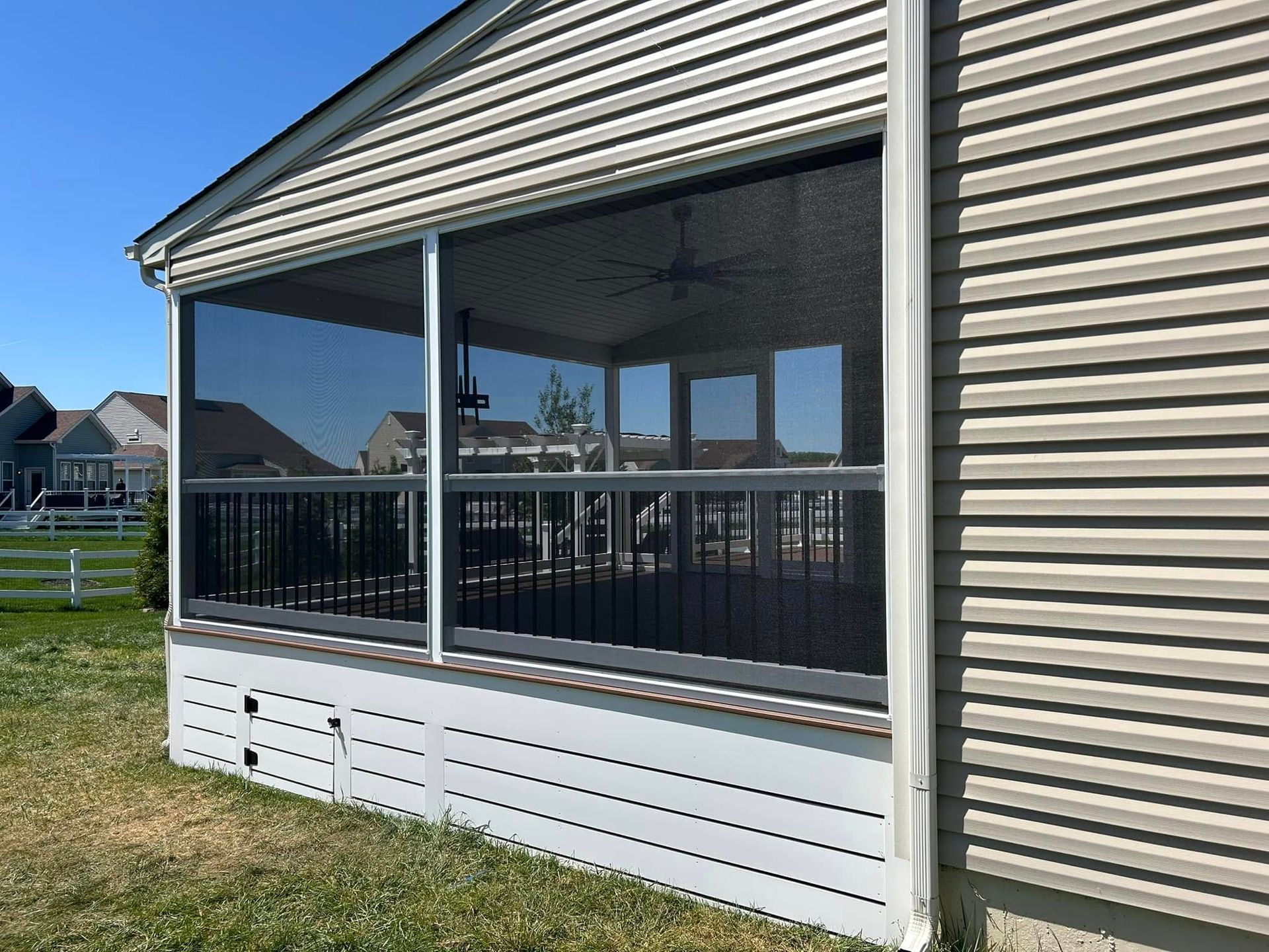 Screened-in porch attached to a house. Features dark screens, black railing, and beige siding.