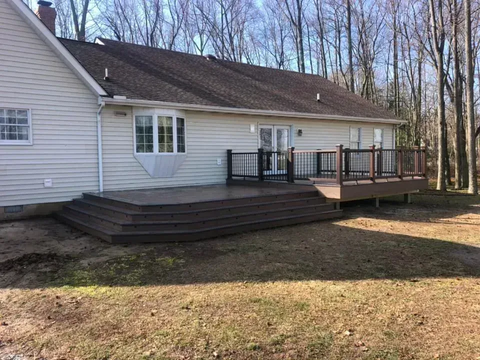 Back view of a house with a multi-level composite deck, dark brown steps and railings, in a grassy backyard.