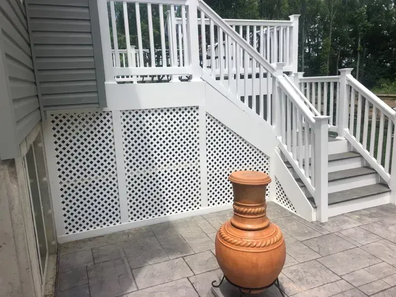 White deck with stairs, lattice skirting, and large brown urn on a stone patio.