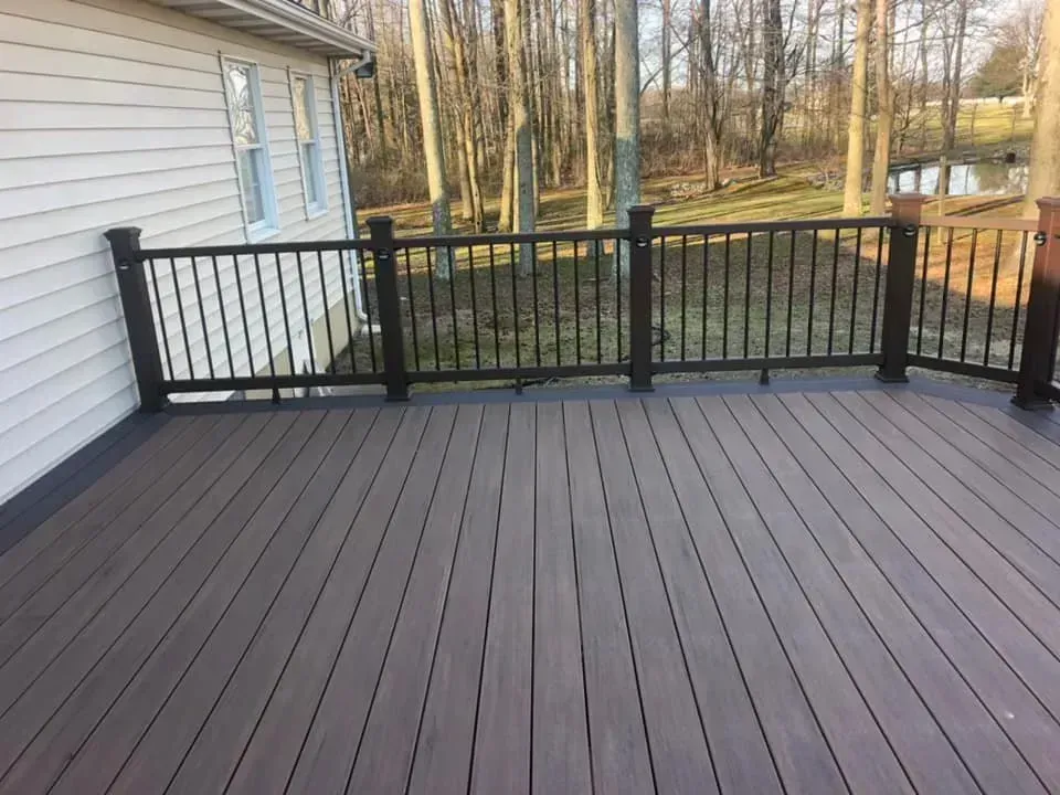 Brown composite deck with black railing overlooking wooded area.
