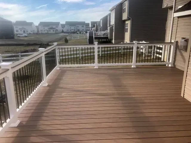 Brown composite deck with white railing posts and black spindles; view of neighborhood in background.