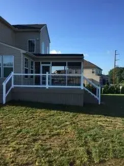 Backyard deck with white railing, screened-in porch, and beige house on a sunny day.