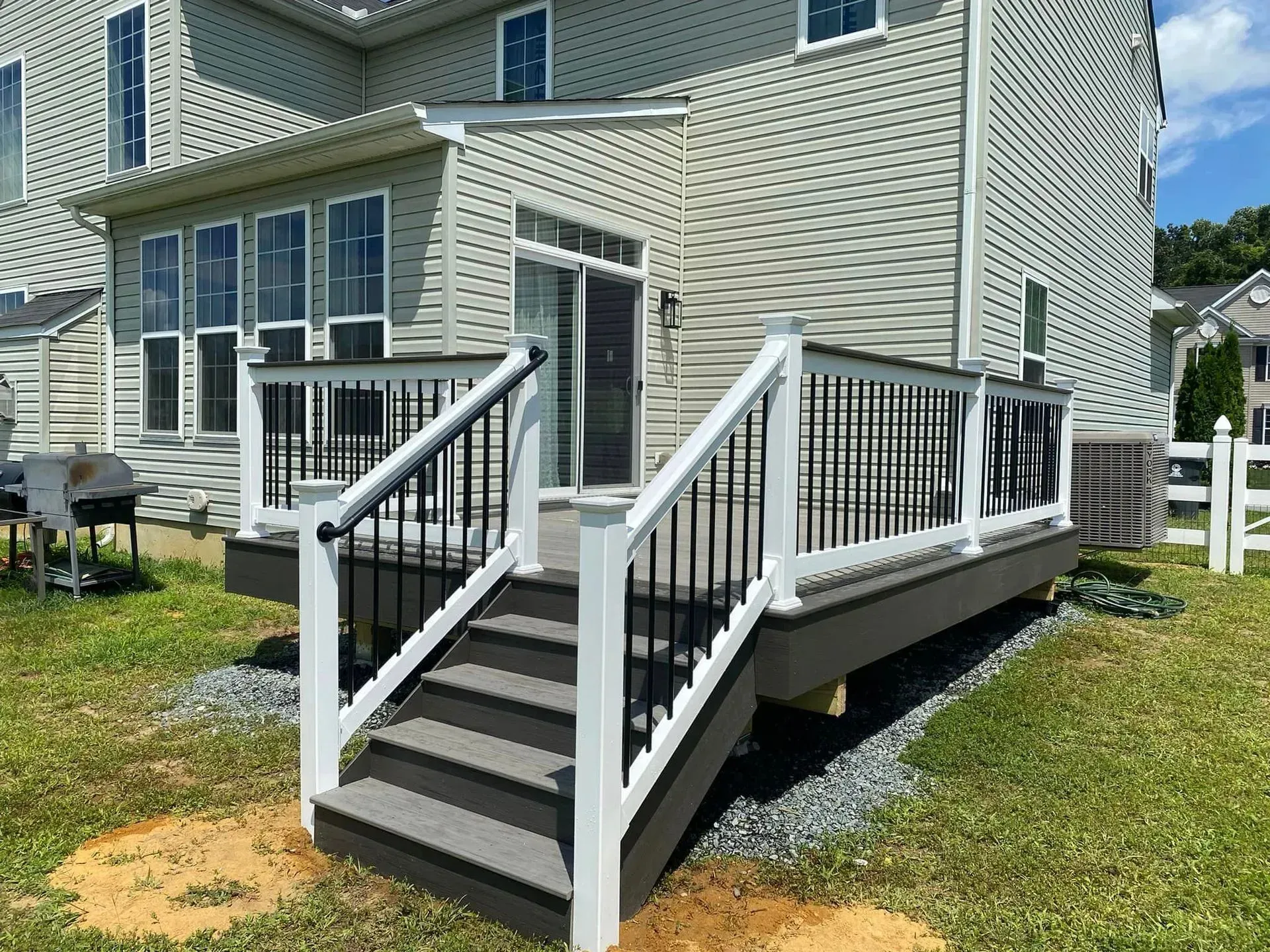 Deck with white railings, black balusters, and gray steps and flooring, next to a house with siding.