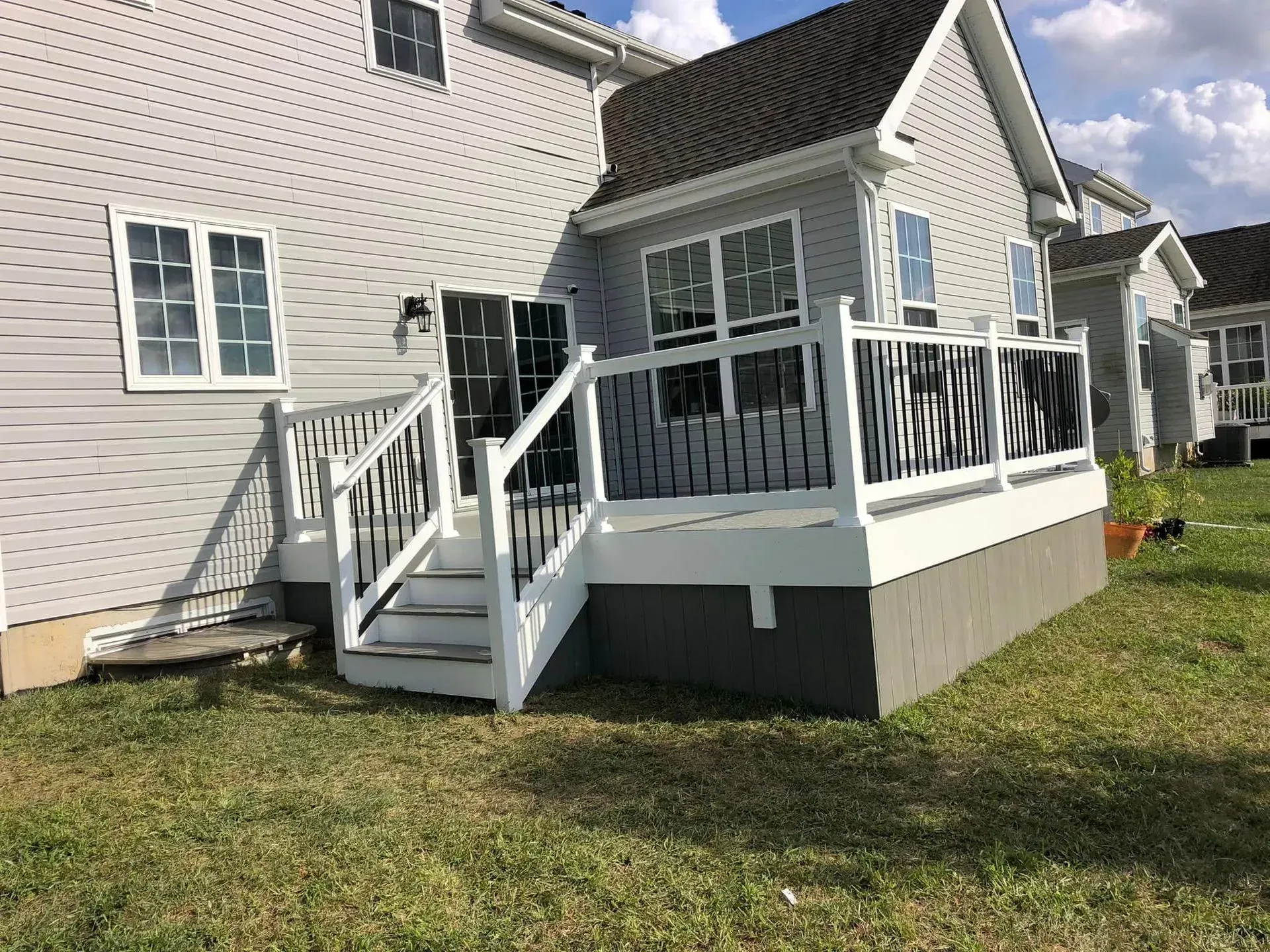 Backyard deck attached to a gray house, with white railing and steps.