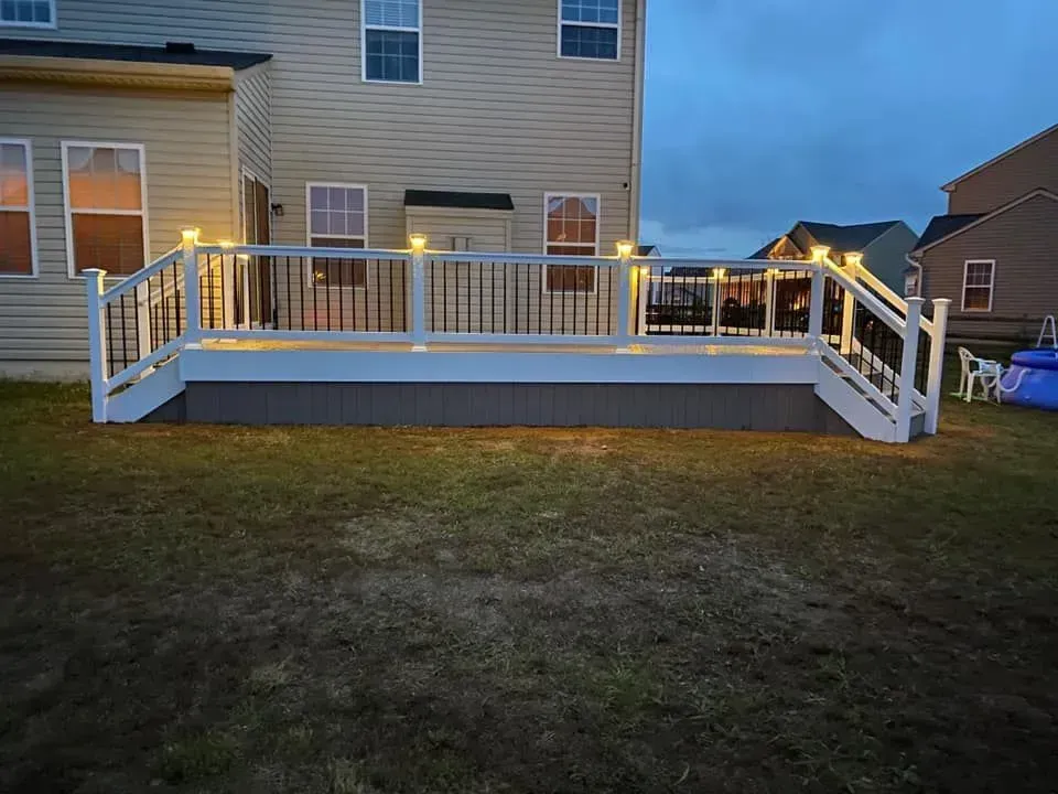 A backyard deck at dusk, with white railings, built-in lights, and dark gray siding.