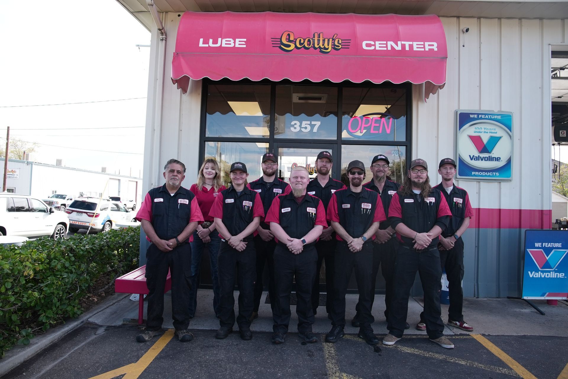 Staff of Lube Center posing outside storefront with awning. Valvoline sign visible.