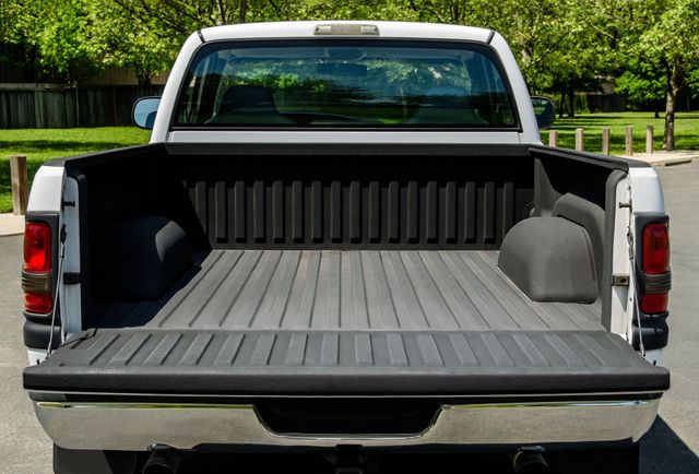 Rear view of a white pickup truck with an empty black truck bed, parked outdoors.