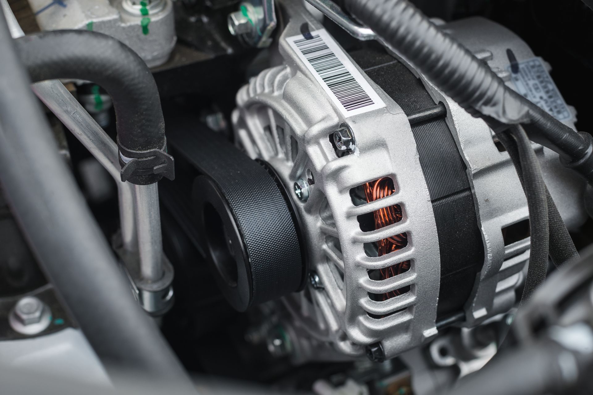 Car engine close-up showing an alternator with a black belt connected to it.