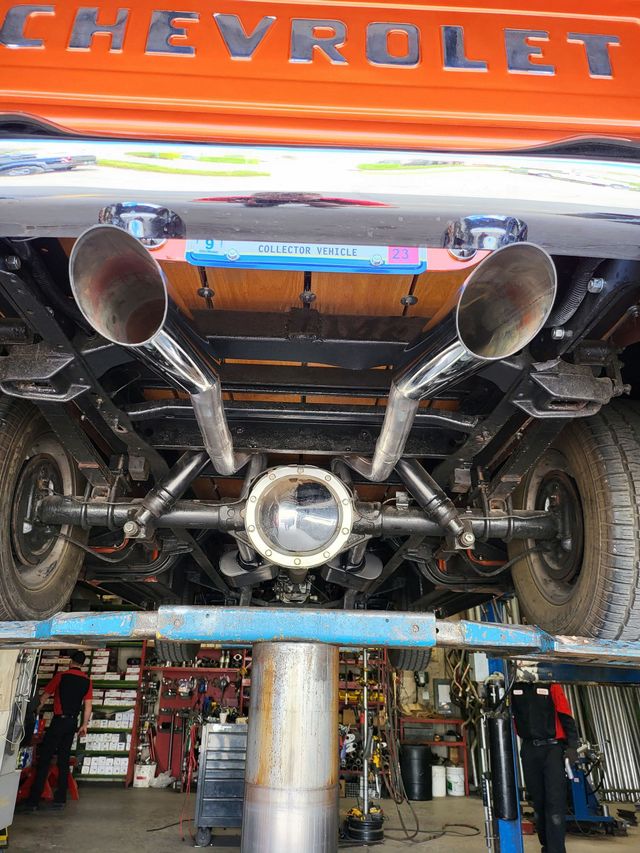Underside view of an orange Chevrolet truck on a lift, showing custom exhaust, axles, and undercarriage details.