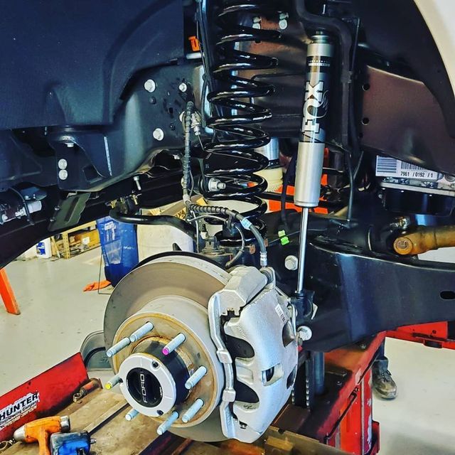 Suspension of a vehicle being worked on; with spring, shock, brake, and other parts visible.