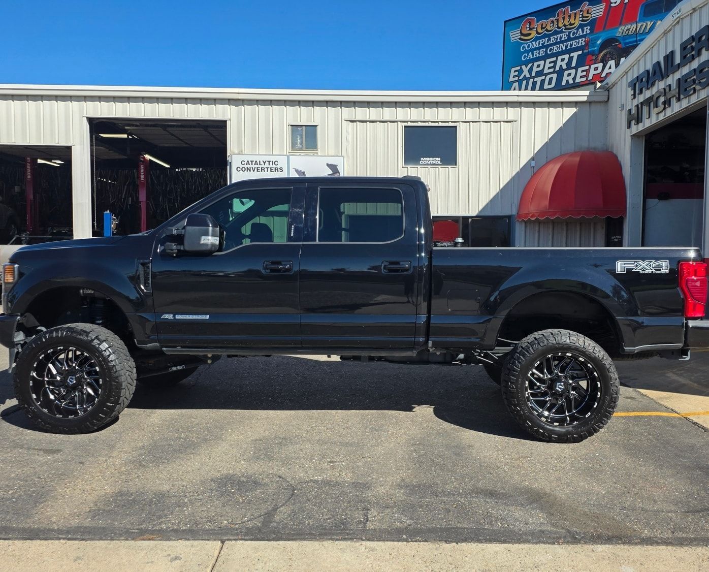 Black lifted Ford pickup truck parked in front of an auto repair shop with black wheels.