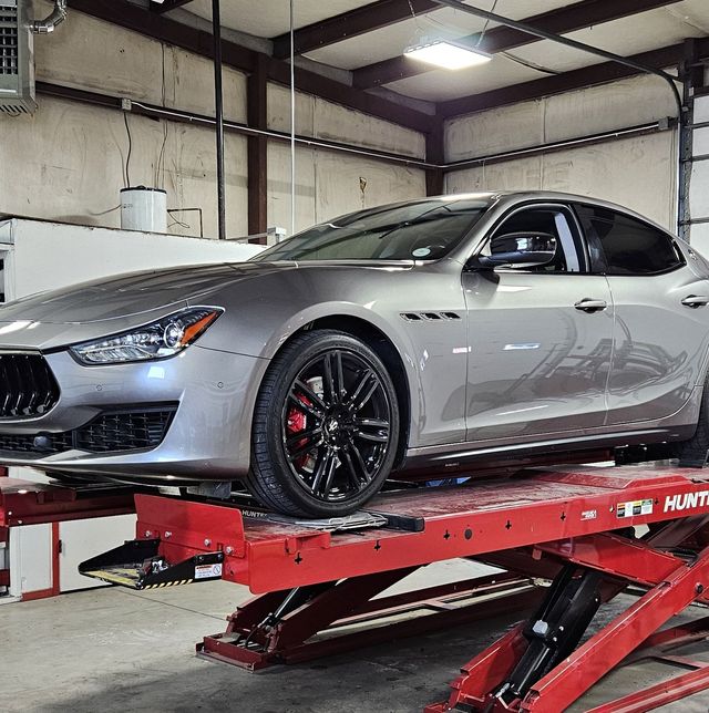 Silver Maserati sedan on a red lift in an auto shop. Black wheels, red calipers.