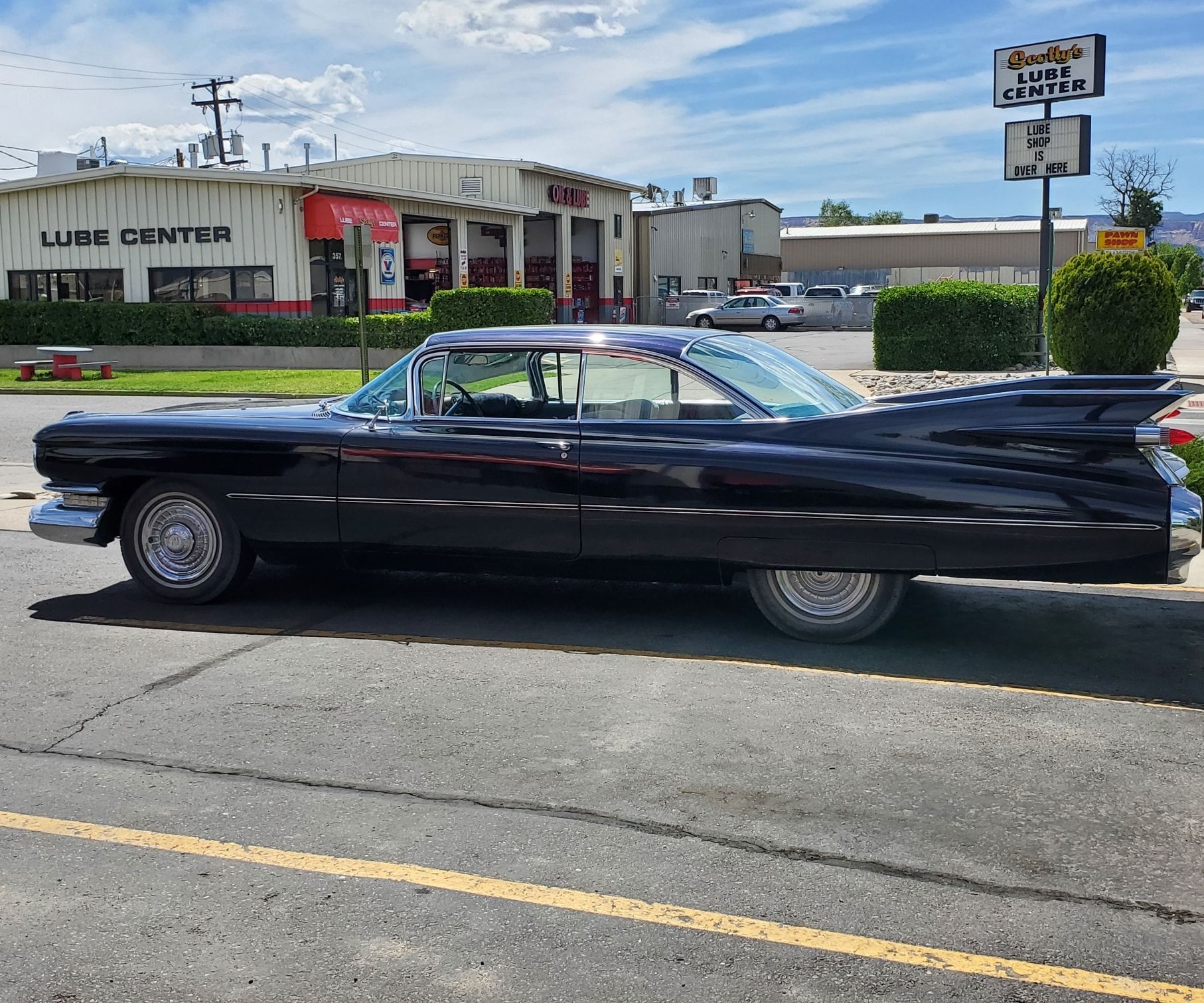 Black classic Cadillac parked on a street in front of a repair shop on a sunny day.