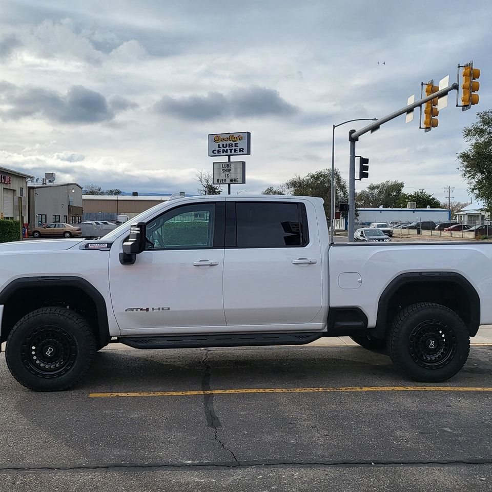 White pickup truck parked on street, black wheels, cloudy sky, traffic lights.