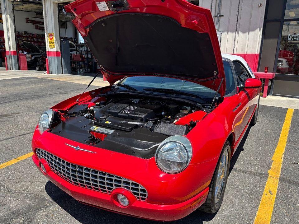 Red Ford Thunderbird with the hood open in a garage, showcasing engine components.