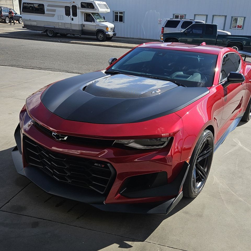 Red Chevrolet Camaro with a black hood parked in front of a white building.