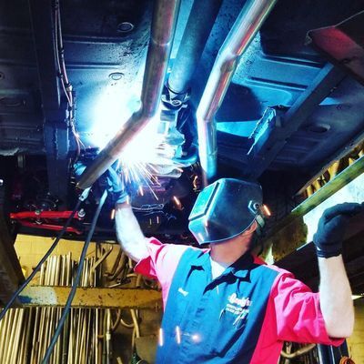 Mechanic welding exhaust pipes under a car, sparks flying.