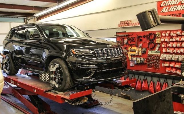 Black Jeep SUV on a red car lift in a garage, undergoing a wheel alignment check.