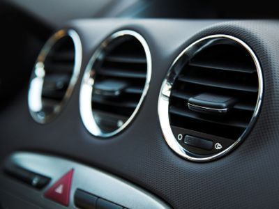 Close-up of three circular air vents in a car dashboard. Chrome trim, black dashboard, and red hazard button.