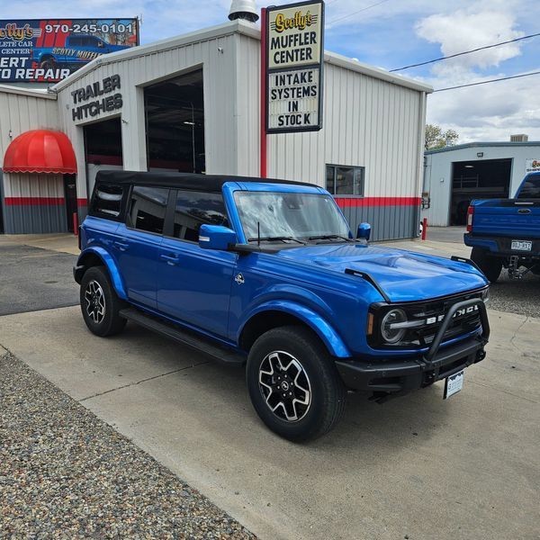 Blue Ford Bronco parked in front of a muffler shop.