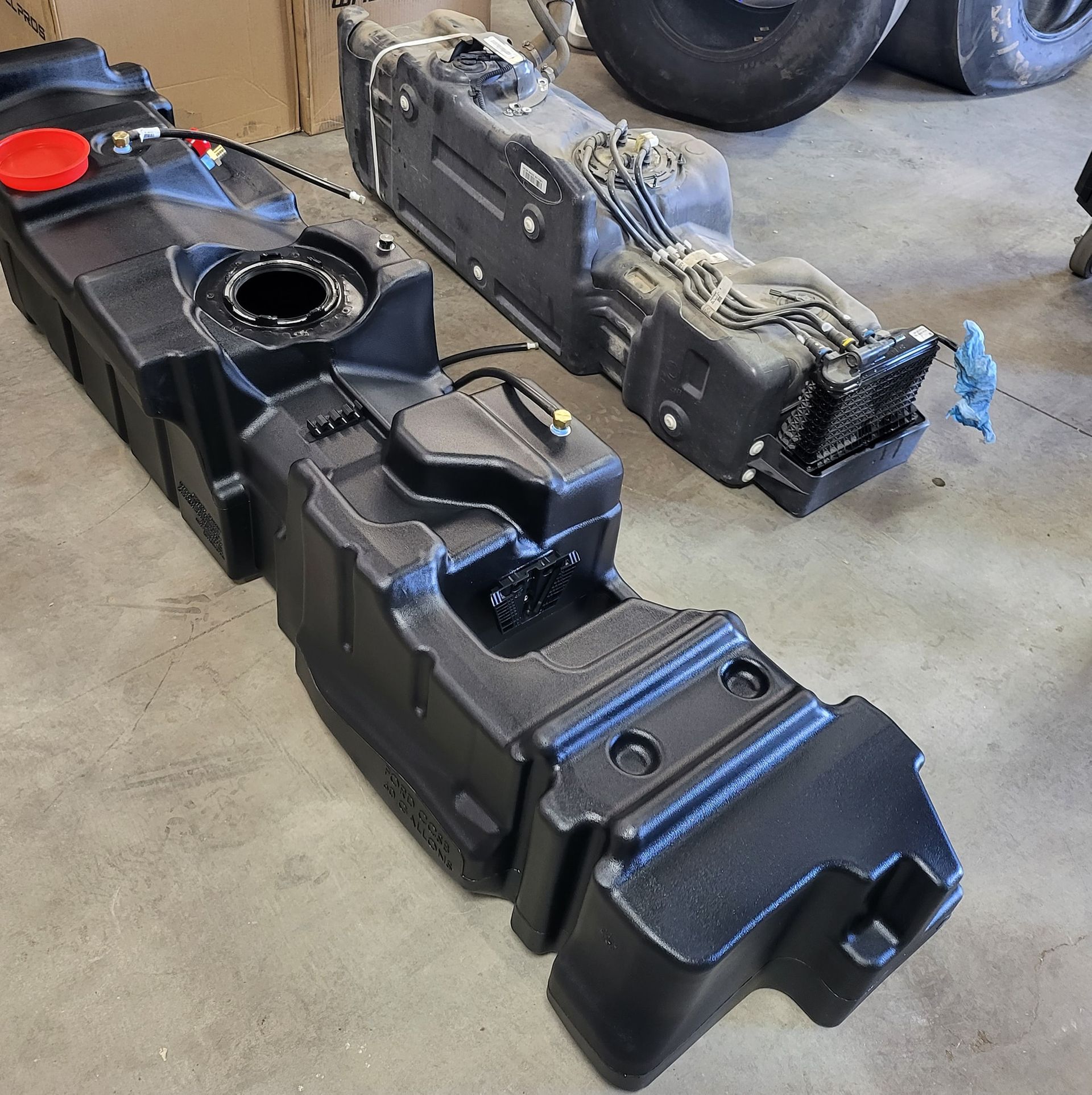 Two black plastic fuel tanks on a concrete floor. One tank has a red cap.