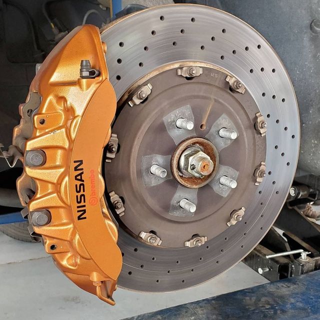 Close-up of a Nissan GT-R gold brake caliper and drilled rotor, mounted on a car.