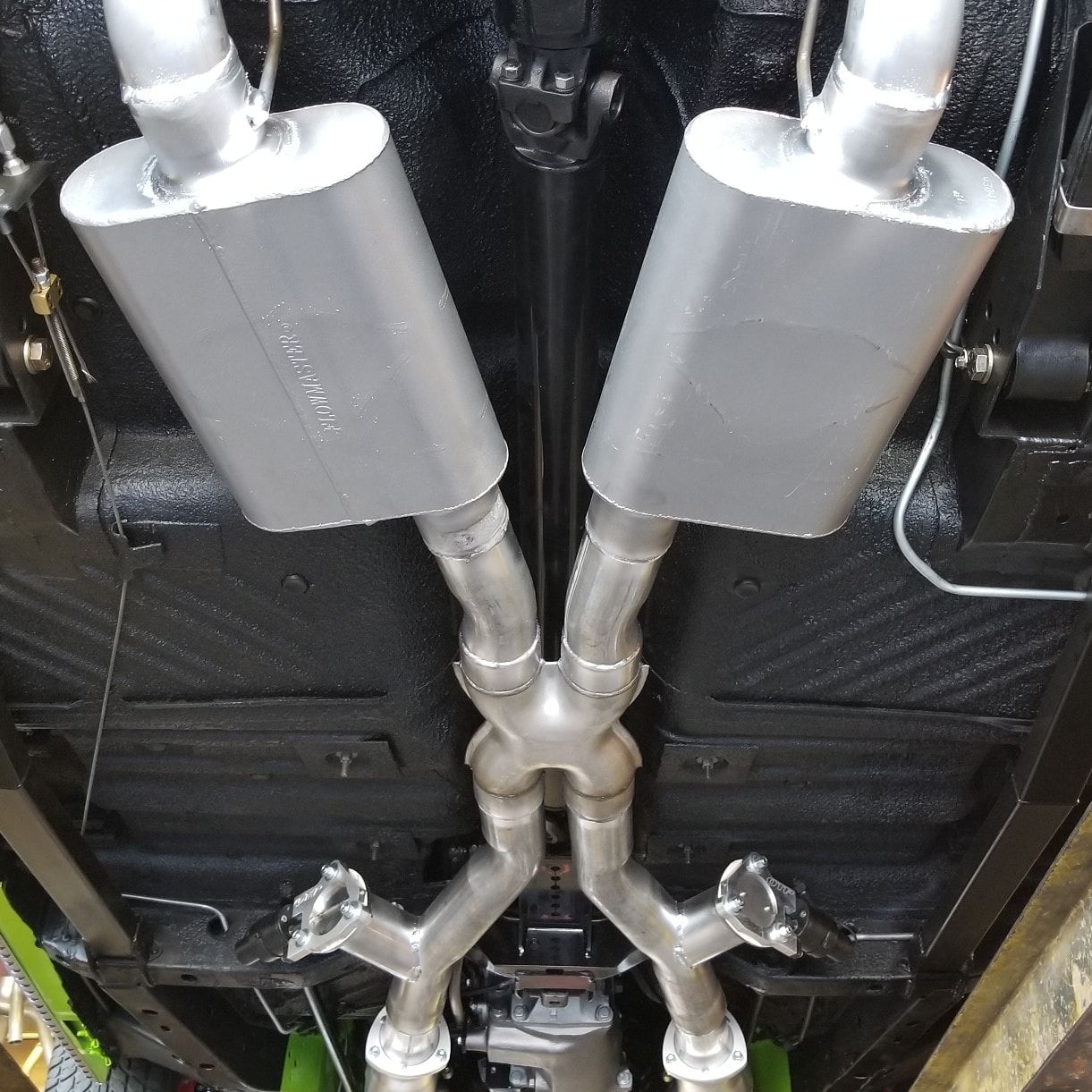 Underside of a classic car showing a dual exhaust system with silver mufflers and pipes.