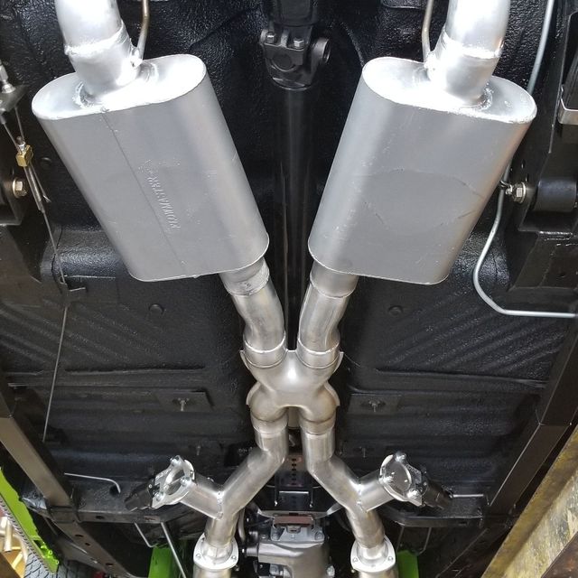 Underside of a classic car showing a dual exhaust system with silver mufflers and pipes.