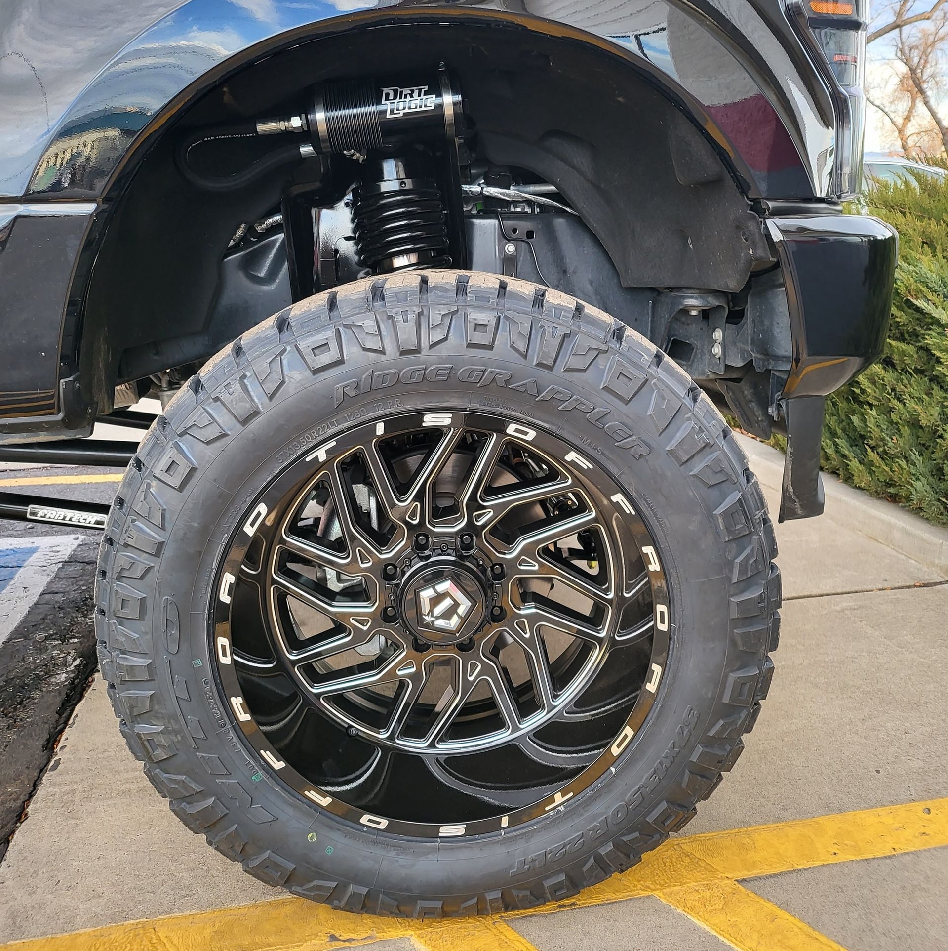 Black truck wheel with black and silver rim, parked near a yellow stripe.
