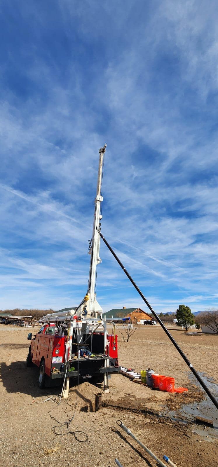 A red truck is parked in a dirt field next to a drilling rig.