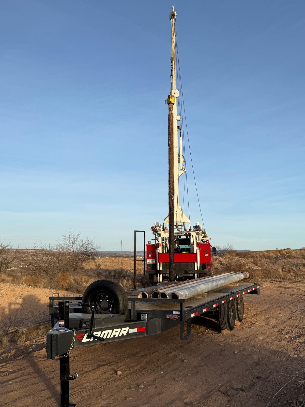 A trailer with a crane on it is parked on the side of a dirt road.
